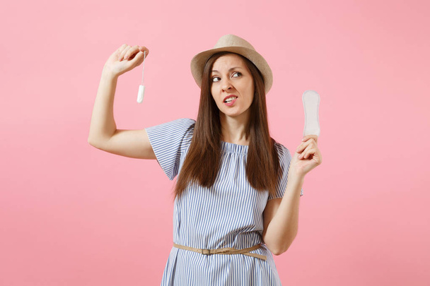 Portrait of young woman in blue dress holding sanitary napkin, tampon for variant safety menstruation days isolated on pink background. Medical healthcare, gynecological, choice concept. Copy space - 写真・画像