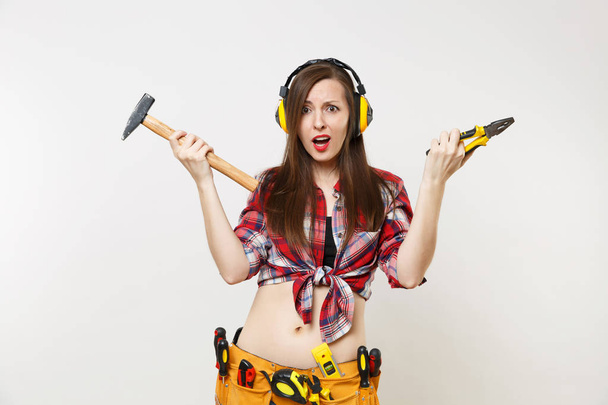 Strong fun young handyman woman in plaid top shirt, denim shorts, noise insulated headphones, kit tools belt full of instruments isolated on white background. Female in male work. Repair home concept - Photo, Image
