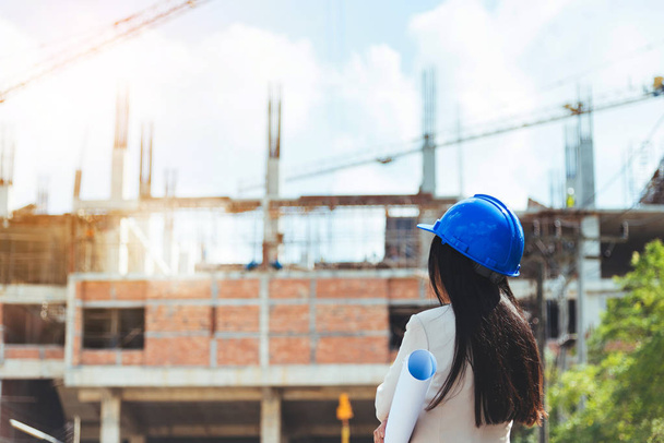 Asian woman architect wearing blue safety helmet checking working progress at contruction site. - Foto, imagen