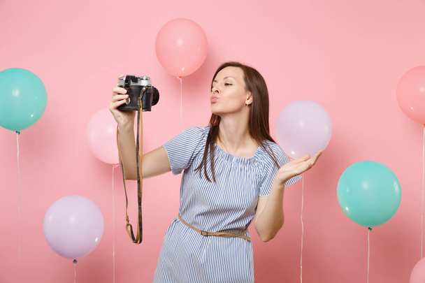 Retrato de tierna mujer feliz en vestido azul hacer selfie en la cámara de fotos retro vintage soplado labios besándose sobre fondo rosa con globos de aire de colores. Fiesta de cumpleaños gente emociones sinceras
 - Foto, Imagen