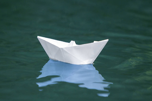 Gros plan d'un simple petit bateau en papier origami blanc flottant tranquillement dans une rivière bleu clair ou de l'eau de mer sous un ciel d'été lumineux. Liberté, rêve et fantasmes concept, fond copyspace
. - Photo, image