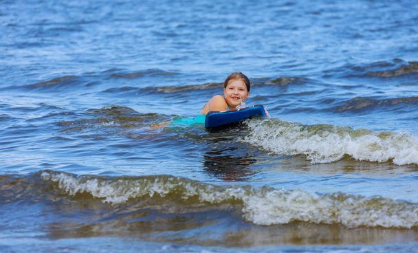 Schattige kleine baby meisje jonge surfer met bodyboarden een plezier op kleine oceaan golven. Actieve familie levensstijl - Foto, afbeelding