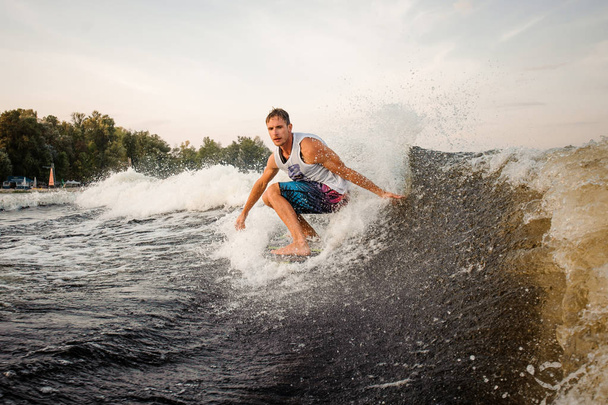 Young active man riding on the wakeboard on high wave of motorboat, having healthy summertime on the open air - Photo, Image