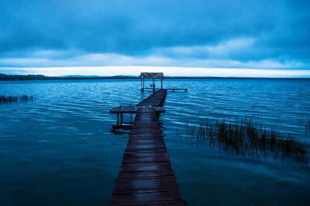 青、エル ・ Remate、グアテマラのペテンで日没前に湖の岸に沿ってドックの後ろに青い cloudscape - 写真・画像