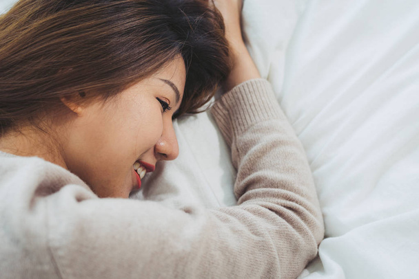 Portrét krásné mladé asijské ženy na posteli doma ráno. Veselá Asijské žena na sobě pohodlný svetr a usmívá se na posteli. Relaxační místnost. životní styl Asie žena domácí koncept. - Fotografie, Obrázek