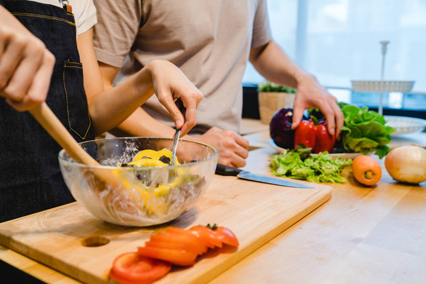 Asian woman prepare salad food in the kitchen. Beautiful happy asian couple are cooking in the kitchen. Young asian couple have romantic time while staying at home. Couple lifestyle at home concept. - Foto, immagini