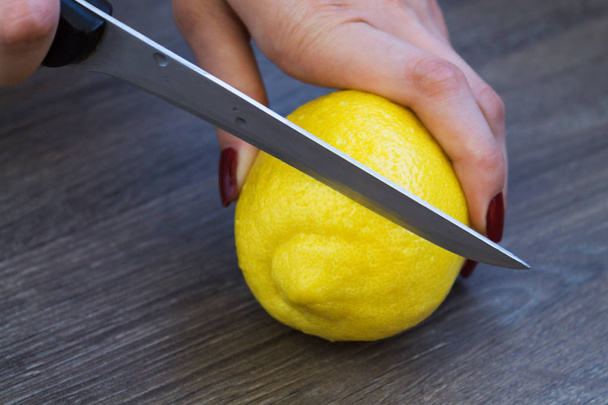 female hands cut a lemon into pieces on a wooden board - Фото, зображення