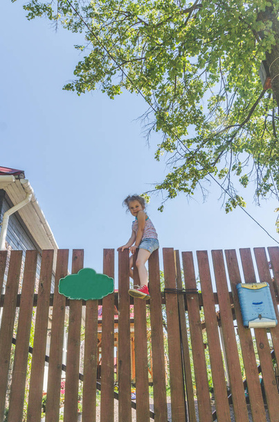 a child, a girl climbs a wooden fence in the village - Fotó, kép