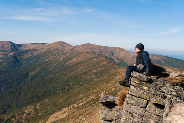 een eenzame toerist geplakt op een steen in het midden van een klif om uit te rusten en bewondert natuur - Foto, afbeelding