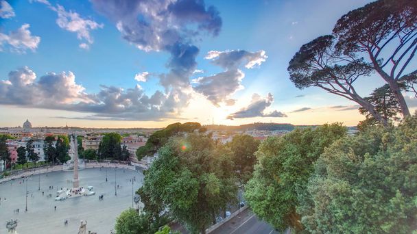 Aerial view of the large urban square, the Piazza del Popolo timelapse, Rome at sunset with the fiery orb of the sun dropping below the horizon above the rooftops of the historical buildings - Foto, imagen