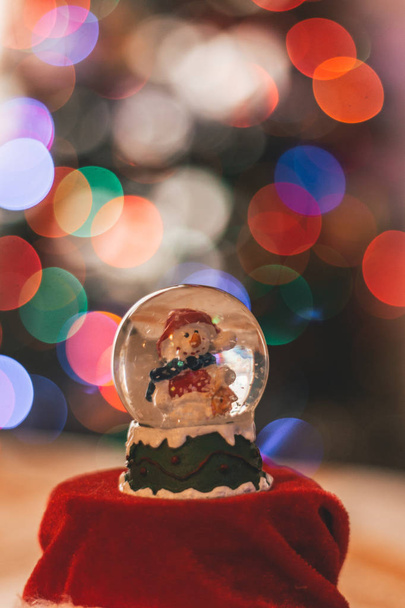 Διακόσμηση μπάλα γυάλινη χιονάνθρωπος με Χριστουγεννιάτικα φώτα που το φόντο εκτός εστίασης - Φωτογραφία, εικόνα