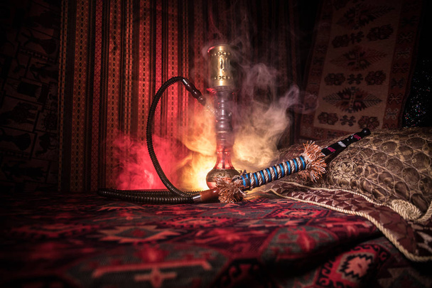 Carvão quente Hookah em shisha tigela fazendo nuvens de vapor no interior da Arábia. Ornamento oriental no tapete. Shisha oriental elegante no escuro com luz de fundo. Para o anúncio da Shisha. Foco seletivo
 - Foto, Imagem