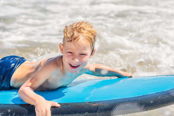 Happy baby boy - young surfer ride on surfboard with fun on sea waves. Active family lifestyle, kids outdoor water sport lessons and swimming activity in surf camp. Summer vacation with child. - Foto, Bild