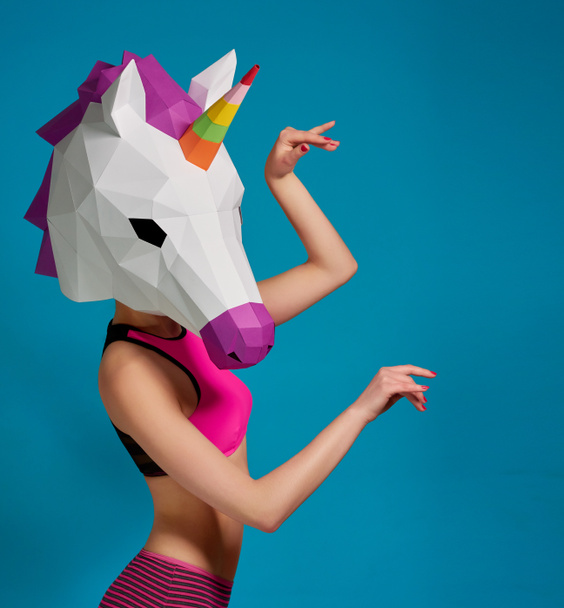 Young girl posing wearing unicorns mask on saturated blue background. - Photo, Image