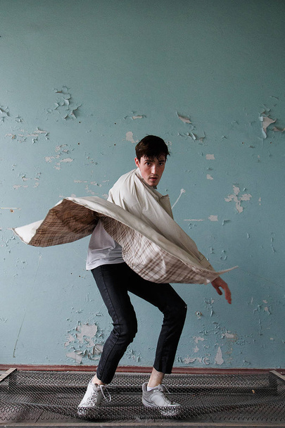 Молодой человек прыгает на старую кровать в плаще и белой рубашке. Мода фото
. - Фото, изображение