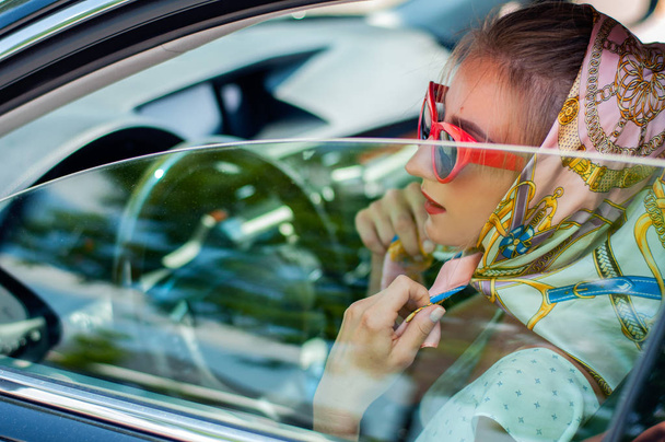 schöne Modefrau mit roten Lippen und Sonnenbrille im Auto sitzend. - Foto, Bild