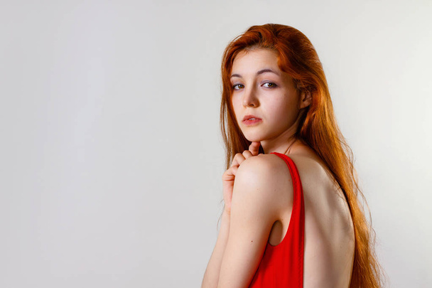 Jeune femme mince sexy en maillot de bain rouge posant en studio. Portrait de mode pleine longueur de belle fille aux longs cheveux roux ondulés. Maillot de bain ou mode bikini. Espace de copie, fond gris
 - Photo, image
