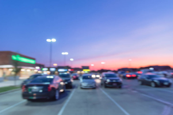Abstrato exterior borrado da tira comercial moderna em Irving, Texas, EUA ao pôr do sol. Linha de centro comercial de carros em estacionamentos ao ar livre descobertos, bokeh da loja de varejo, postes de luz no fundo
 - Foto, Imagem