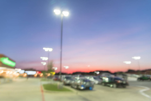 Absztrakt homályos külsejét modern kereskedelmi szalag Irving, Texas, USA, naplementekor. Bevásárlóközpont sor szabadtéri fedetlen parkoló autók kicsiben elad készlet, Lámpaoszlopok, háttérben a bokeh - Fotó, kép