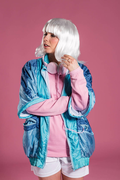 young woman with retro clothes listening to music and dancing against a pink background, studio shot - Foto, Imagem
