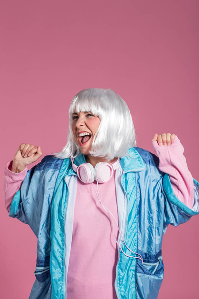 young woman with retro clothes listening to music and dancing against a pink background, studio shot - Фото, изображение