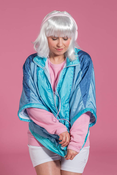 young woman with retro clothes listening to music and dancing against a pink background, studio shot - Photo, Image
