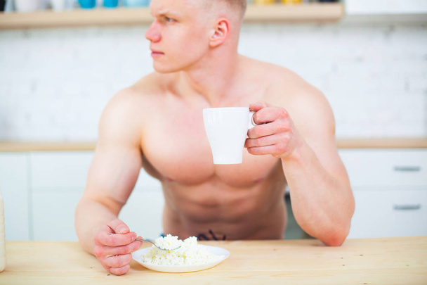 Muscular man with a naked torso in the kitchen with milk and cottage cheese, the concept of a healthy diet. Athletic way of life. - 写真・画像