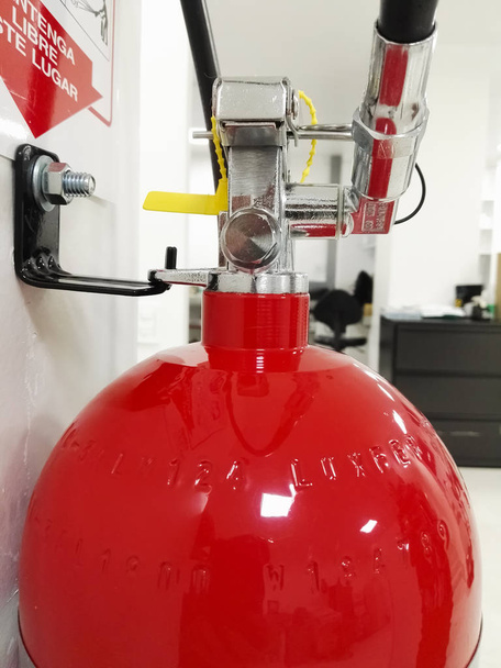 Червоний вогнегасник з деталями запобіжного пристрою, прикріпленого до білої стіни, розташованої в лабораторному або освітленому білому просторі
 - Фото, зображення