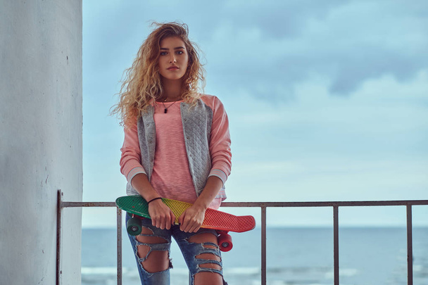 Zmysłowa dziewczyna z blond włosy ubrana w różowy kurtka stojącego obok poręczy z wybrzeżem Morza. - Zdjęcie, obraz