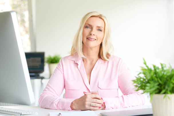 Portrait of smiling businesswoman sitting in light office - Zdjęcie, obraz