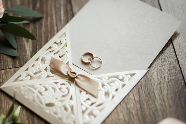 anéis de casamento estão no cartão de convite no fundo de um buquê
 - Foto, Imagem