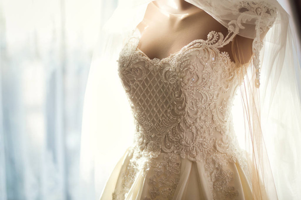 lindo vestido de noiva pendurado no quarto, mulher se preparando antes da cerimônia - Foto, Imagem