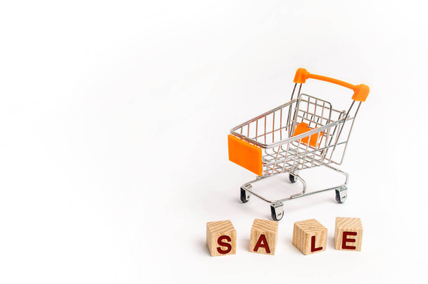 Wooden blocks with the word sale and a supermarket cart on a white background. The concept of sales and seasonal sales of goods and services. Discounts and promotions. Place for text. - Фото, зображення