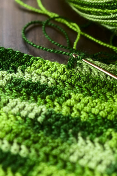 Artesanato de crochê, fazendo um tapete de lugar de fios verdes com um padrão de pontos duplos usando um gancho de crochê de metal ou agulha, fotografado com luz natural (Foco seletivo, Foco no gancho da agulha
) - Foto, Imagem