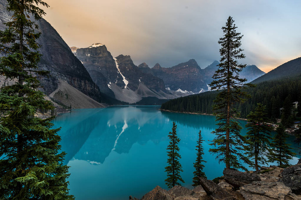 Ανατολή του ηλίου με τα γαλαζοπράσινα νερά της λίμνης Moraine με αμαρτία αναμμένα βραχώδη όρη στο εθνικό πάρκο Banff του Καναδά στην κοιλάδα από τις δέκα κορυφές. - Φωτογραφία, εικόνα