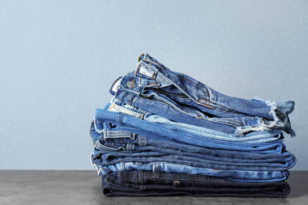 Stack of jeans on table against grey background - 写真・画像