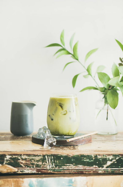 Iced matcha latte drink in glass, white wall and plant branches at background - Photo, image
