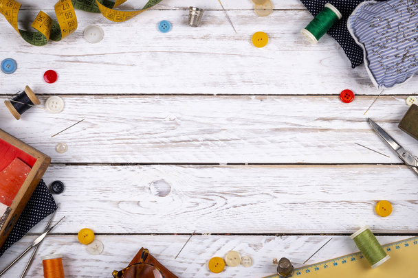 Hermoso conjunto de tijeras de metal de mesa de madera blanca dispersas, botones surtidos y carretes de costura con hilos de colores y cinta métrica desde arriba
 - Foto, Imagen