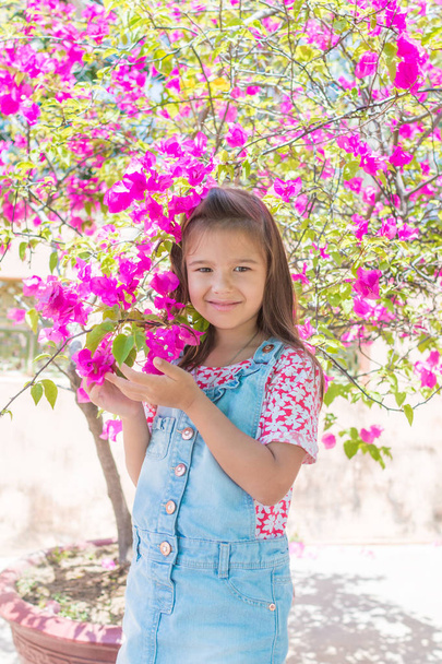 An adorable one little girl stands next to a large bush of pink flowers, bougainvillea - Fotografie, Obrázek