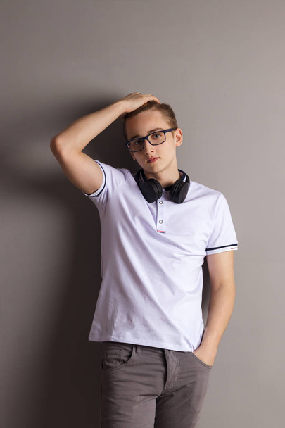 Handsome boy teenager with headphones stands near wall in grey studio - Photo, Image