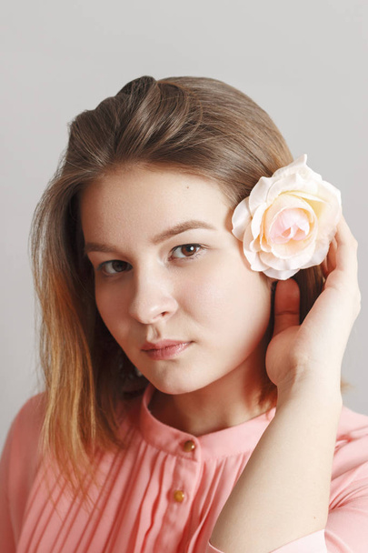 Cute girl teenager in pink dress poses with white rose in hair in studio - Фото, зображення