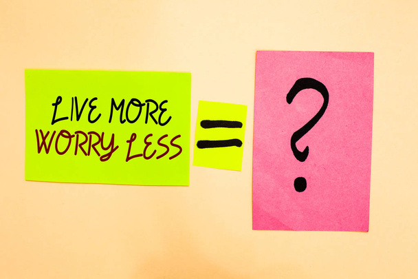 Пишу записку, показывающую Live More Worry Less. Хорошее отношение мотивация быть небрежным наслаждаться жизнью Написано на зеленой липкой ноте на желтый и вопросительный знак на розовой бумаге
 - Фото, изображение