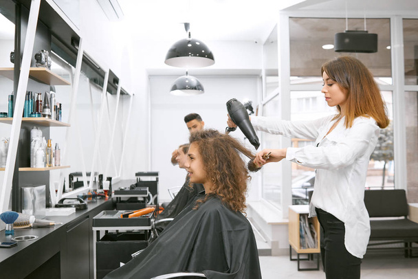 Female hairstylist drying curly girls hair using big plastic brush. - 写真・画像