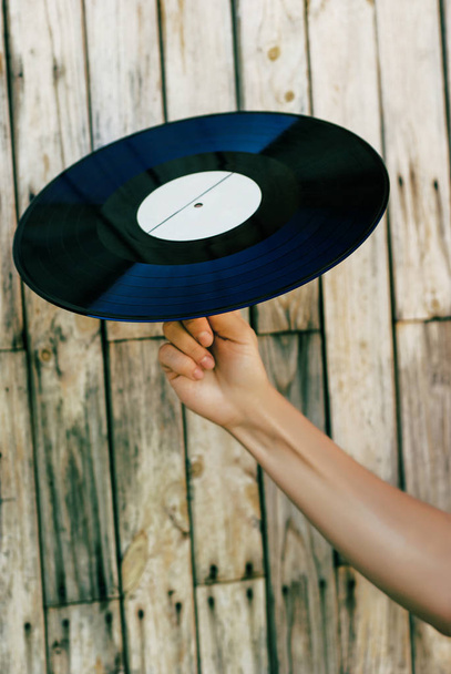 Mano femenina sosteniendo disco de vinilo sobre fondo de madera
 - Foto, Imagen