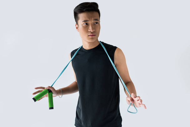 serious young asian sportsman standing jump rope isolated on grey background  - Φωτογραφία, εικόνα