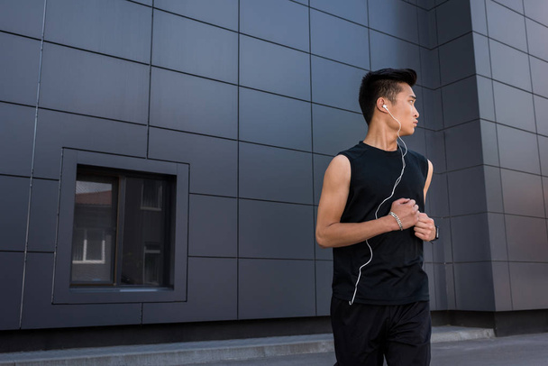 young asian sportsman in earphones running at urban street - Photo, Image