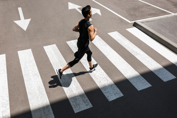 magas, szög, kilátás a fiatal ázsiai sportoló a fülhallgató futás-on város utca - Fotó, kép