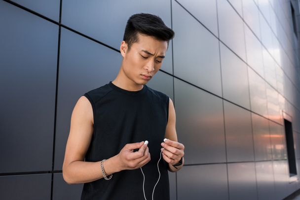 sério jovem asiático desportista colocando em fones de ouvido na cidade rua
 - Foto, Imagem