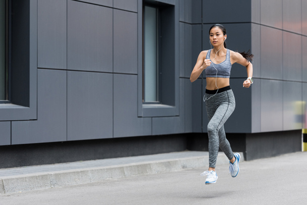 atractivo joven asiático sportswoman en auriculares corriendo en ciudad calle
 - Foto, Imagen