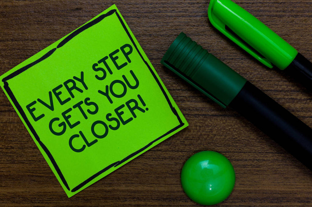 Text sign showing Every Step Gets You Closer. Conceptual photo Keep moving to reach your goals objectives Written on sticky note two markers laid on wooden floor green ball - Photo, Image